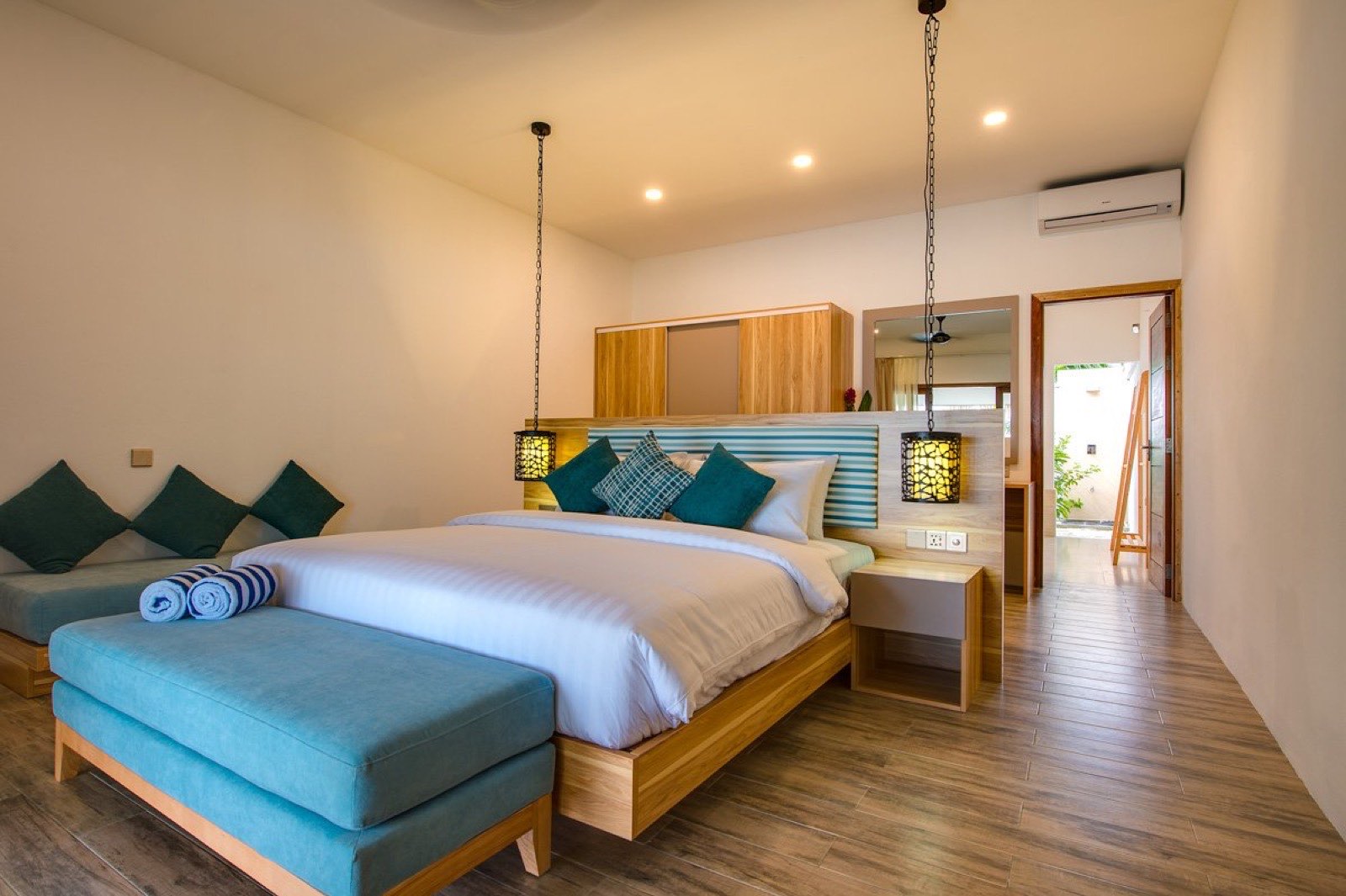 Interior of a Lagoon View Villa with a large bed, timber ceiling and doors opening to the light outside.